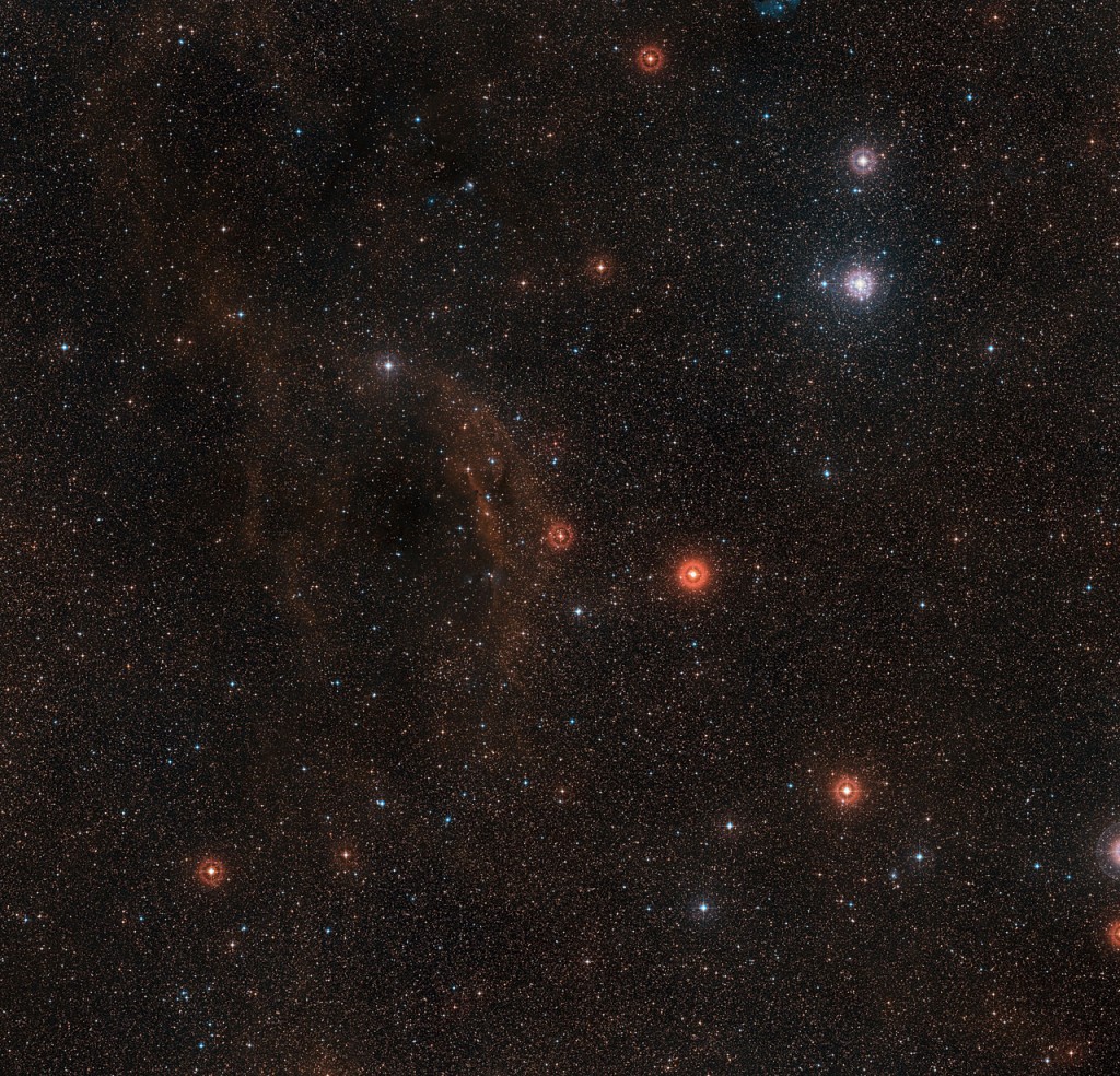 This wide-field view shows the sky around the very brilliant red hypergiant star VY Canis Majoris, one of the largest stars known in the Milky Way. The star itself appears at the centre of the picture, which also includes clouds of glowing red hydrogen gas, dust clouds and the bright star cluster around the bright star Tau Canis Majoris towards the upper right. This picture was created from images forming part of the Digitized Sky Survey 2.