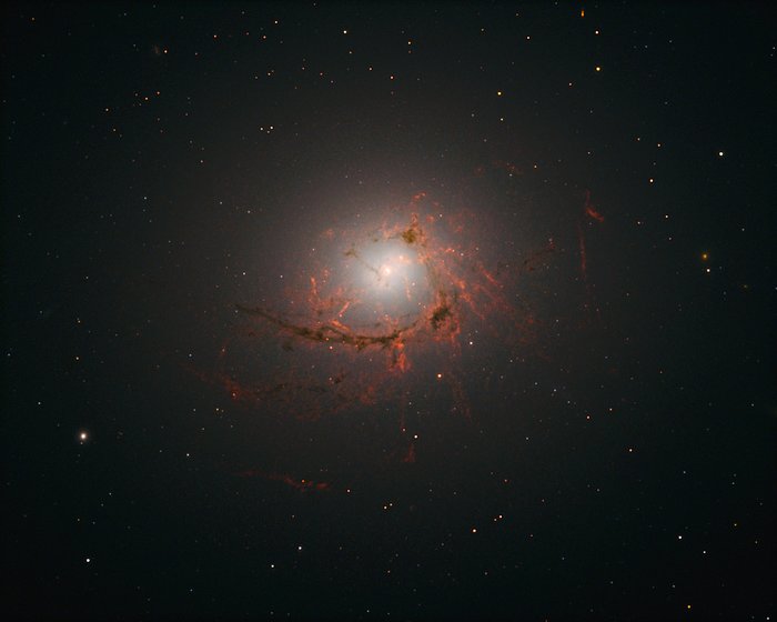 This picture, taken by Hubble’s Wide Field Camera 3 (WFC3), shows NGC 4696, the largest galaxy in the Centaurus Cluster. The new images taken with Hubble show the dusty filaments surrounding the centre of this huge galaxy in greater detail than ever before. These filaments loop and curl inwards in an intriguing spiral shape, swirling around the supermassive black hole at such a distance that they are dragged into and eventually consumed by the black hole itself.